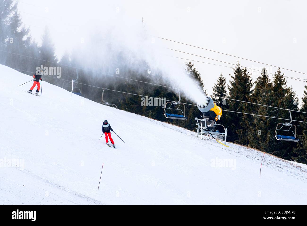 Ruzomberok, Slovaquie - 30 décembre 2025 : machine à neige produisant de la neige artificielle sur les pistes de ski de la station de ski de Malino Brdo pendant que les skieurs descendent, salut Banque D'Images