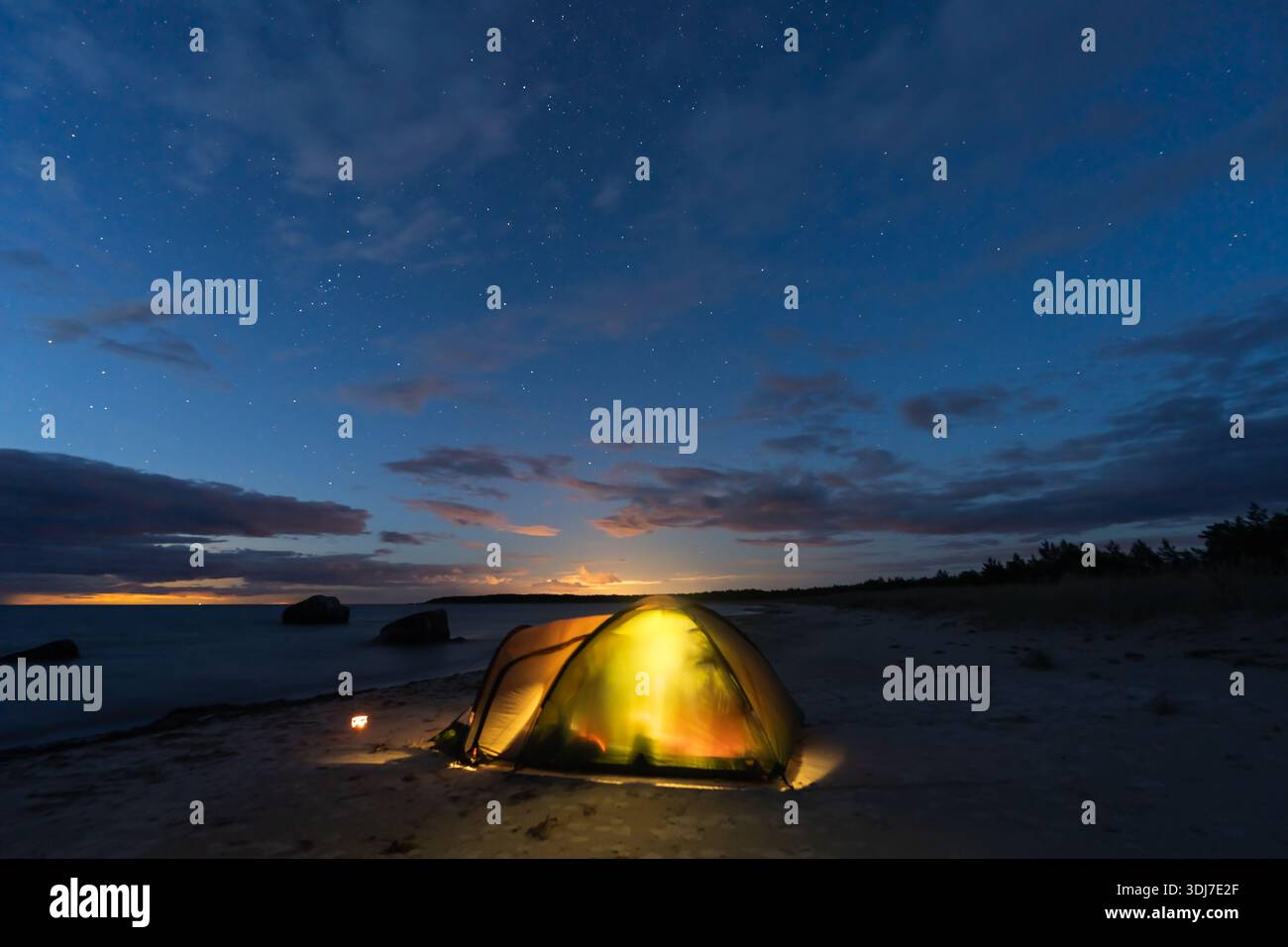 Tente de camping jaune éclatante sur une plage de sable estonienne sous un ciel étoilé crépusculaire avec mer Baltique calme et pierres. Banque D'Images