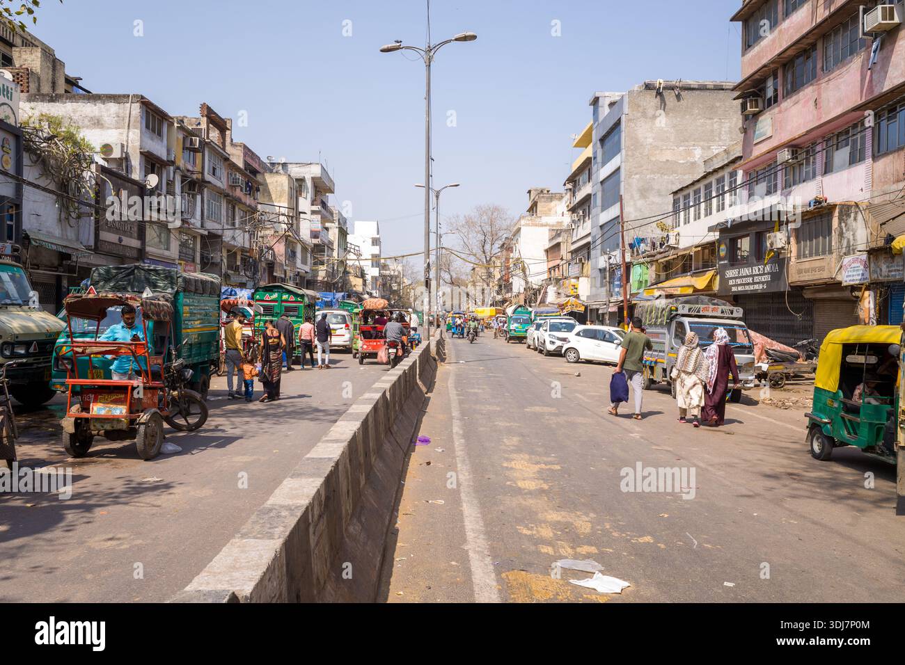 Delhi, Inde - 13 mars 2022 : une rue large dans le bazar de Sadar montre des piétons, des pousse-pousse automobiles, des pousse-pousse à vélo et des véhicules se déplaçant devant des bâtiments commerciaux et résidentiels à plusieurs étages sous un ciel dégagé. Banque D'Images