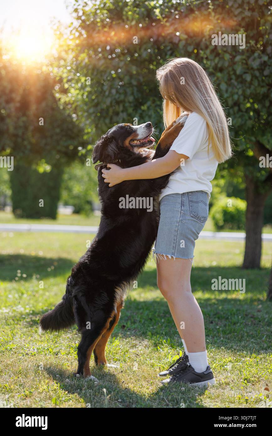 Une femme joyeuse embrasse son grand chien dans un parc ensoleillé avec des arbres et de la verdure, chérissant leur moment ludique ensemble Banque D'Images