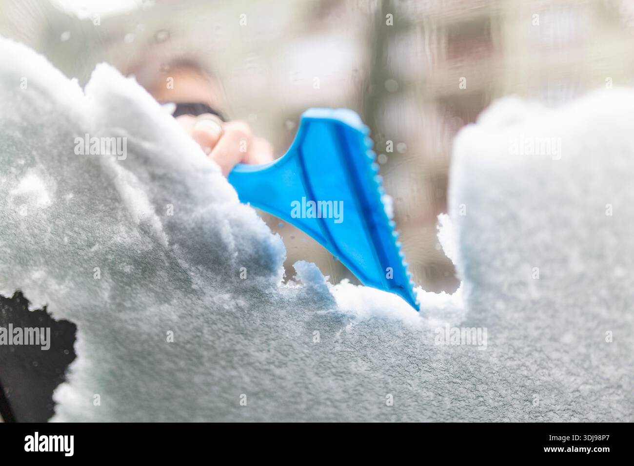La main des femmes enlève la neige du pare-brise de voiture dans la journée d'hiver, nettoyant la voiture de la neige Banque D'Images