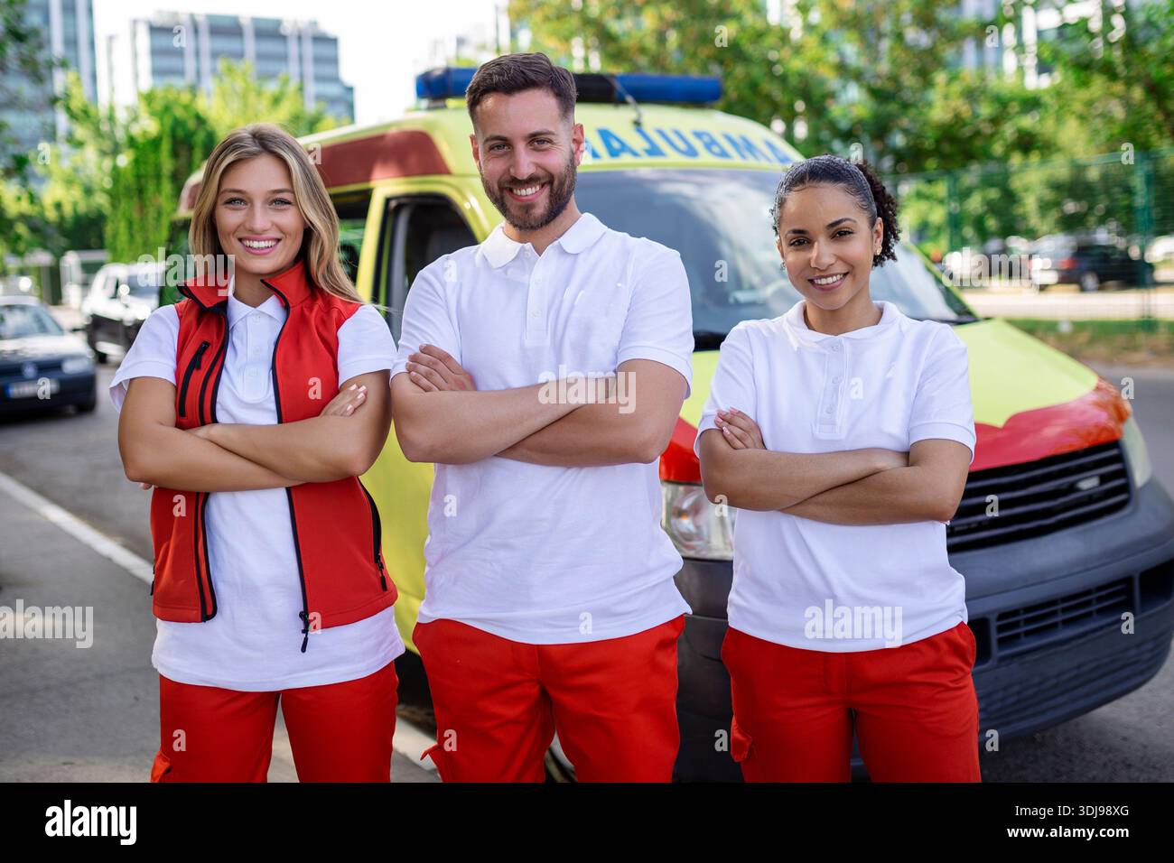 Groupe multiethnique de paramédicaux debout à côté d'une ambulance avec portes ouvertes. Leur collègue portant un sac médical pour traumatismes. Ils sourient Banque D'Images