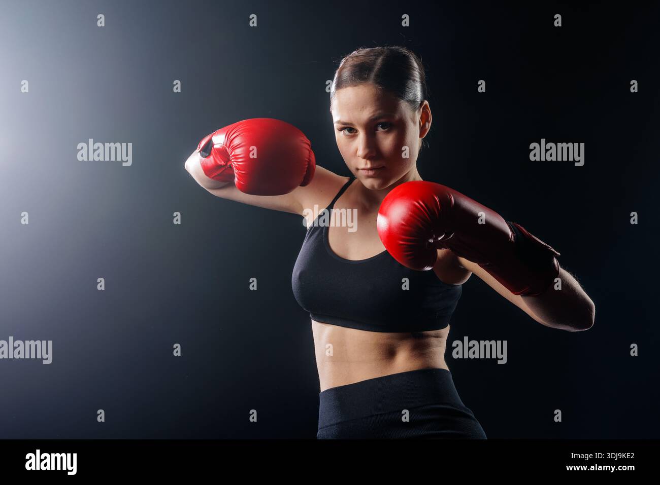 Jeune boxeur féminin dans des gants rouges dans la position de combat sur fond de studio sombre avec espace de copie pour la bannière de site Web ou la publicité sociale. Banque D'Images