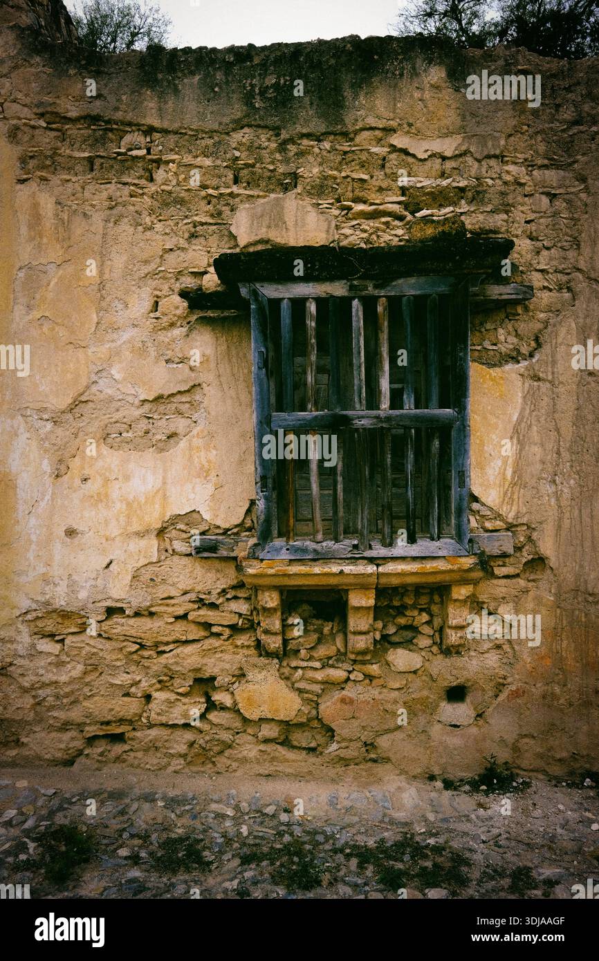 Un mur vieilli et altéré avec une fenêtre en bois rustique avec des barres métalliques, capturant le charme de l'architecture historique Banque D'Images