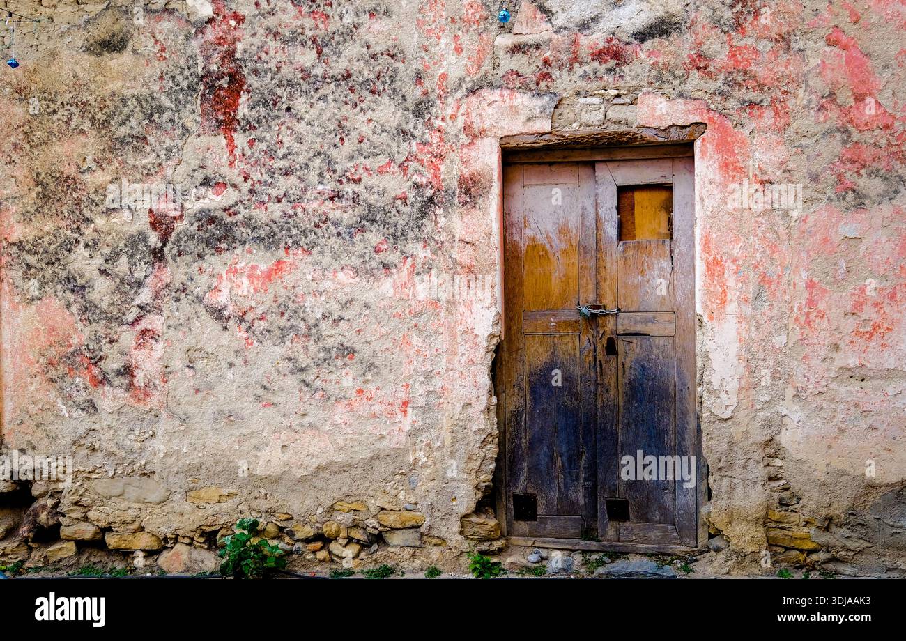 Une vieille porte en bois vieillie avec une serrure rustique, posée contre un mur texturé et délavé orné de peinture écaillée Banque D'Images