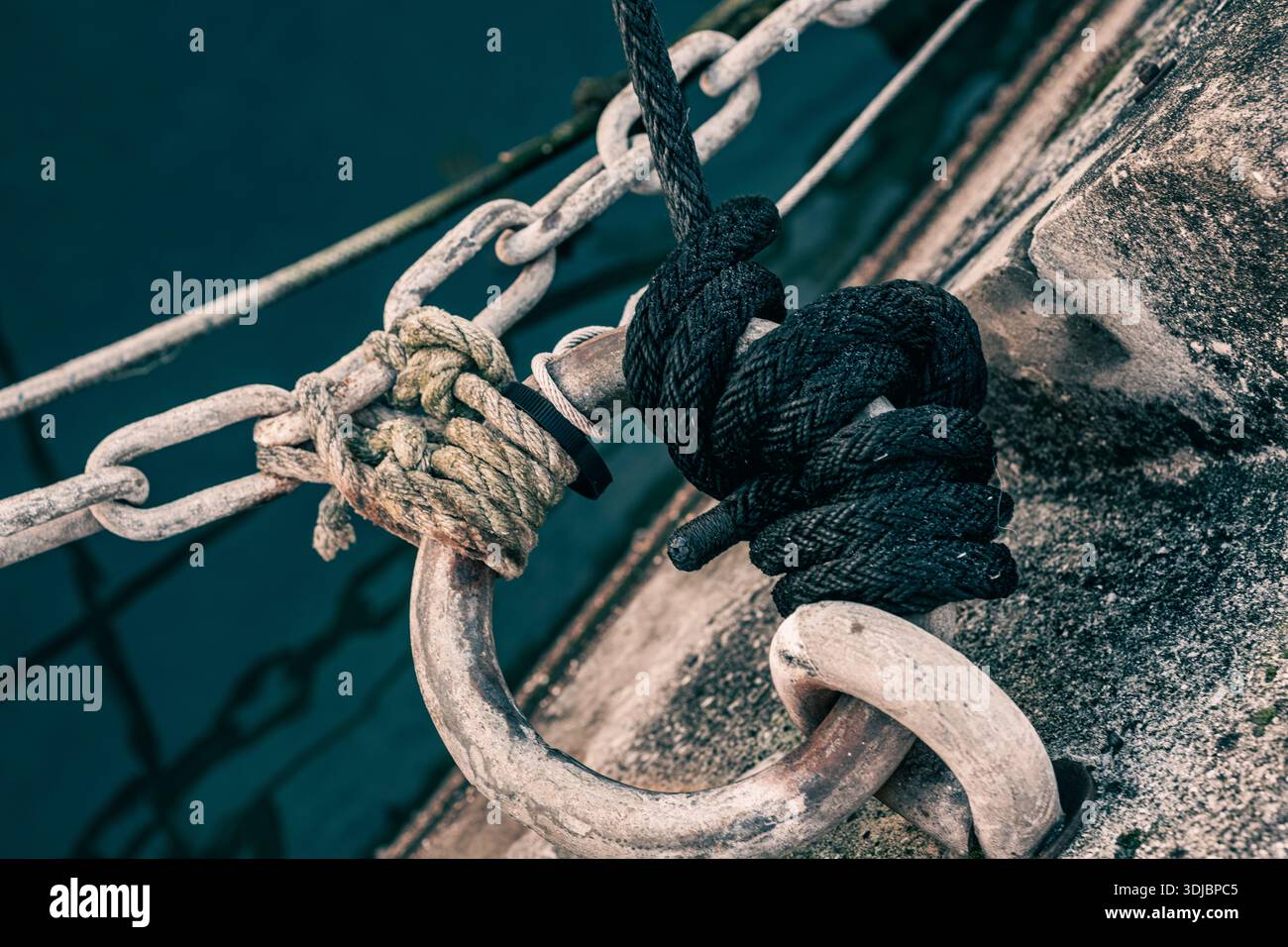 Les chaînes et les cordes sont attachées à des anneaux métalliques encastrés dans le remblai de béton d'une marina. Chaînes d'amarrage, cordes, nœuds et amortisseurs pour l'amarrage Banque D'Images