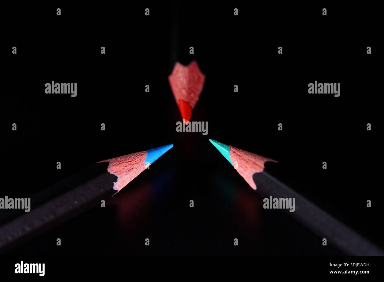 Trois crayons de couleur se réunissant à un point sur fond noir Banque D'Images