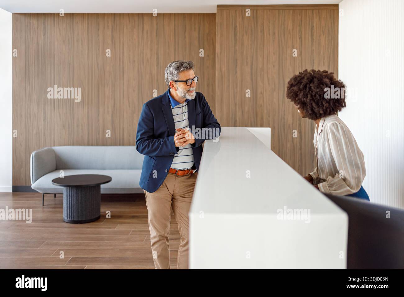 Homme d'affaires d'âge mûr discutant avec la réceptionniste de l'hôtel à la réception concernant la réservation des chambres et les services à la clientèle Banque D'Images