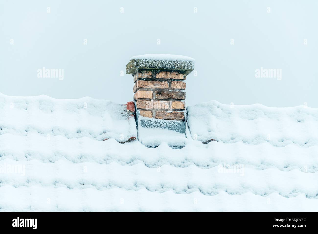 Cheminée en brique enneigée sur le toit contre ciel d'hiver pâle, foyer sélectif Banque D'Images
