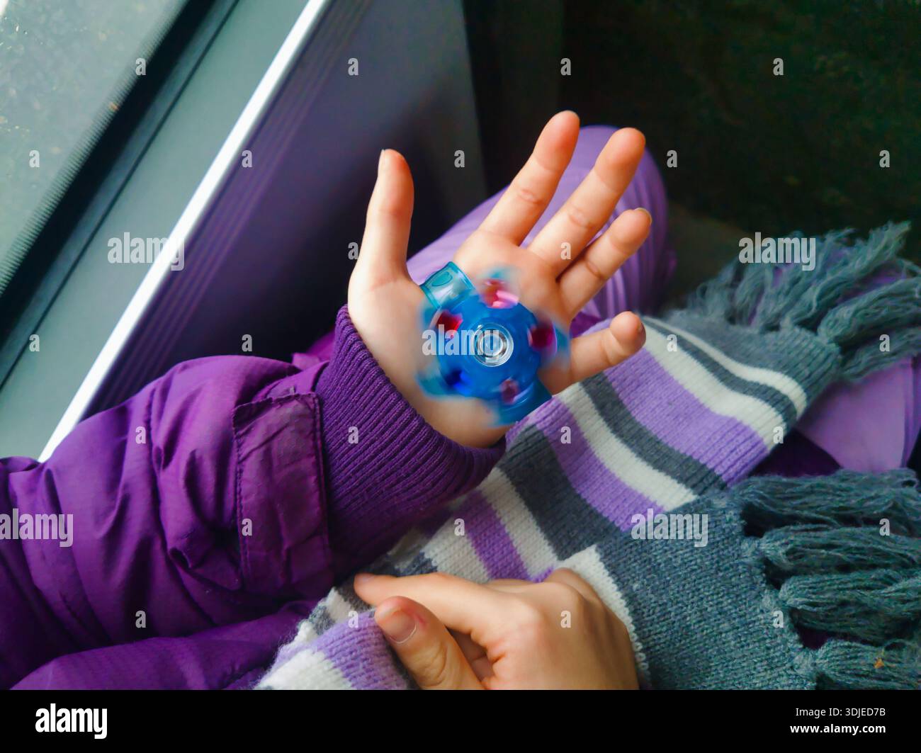 Gros plan de la paume ouverte d'un enfant affichant une montre-jouet LED bleue qui tourne. Le sujet porte une veste d'hiver violette et une écharpe rayée pendant son voyage. Banque D'Images