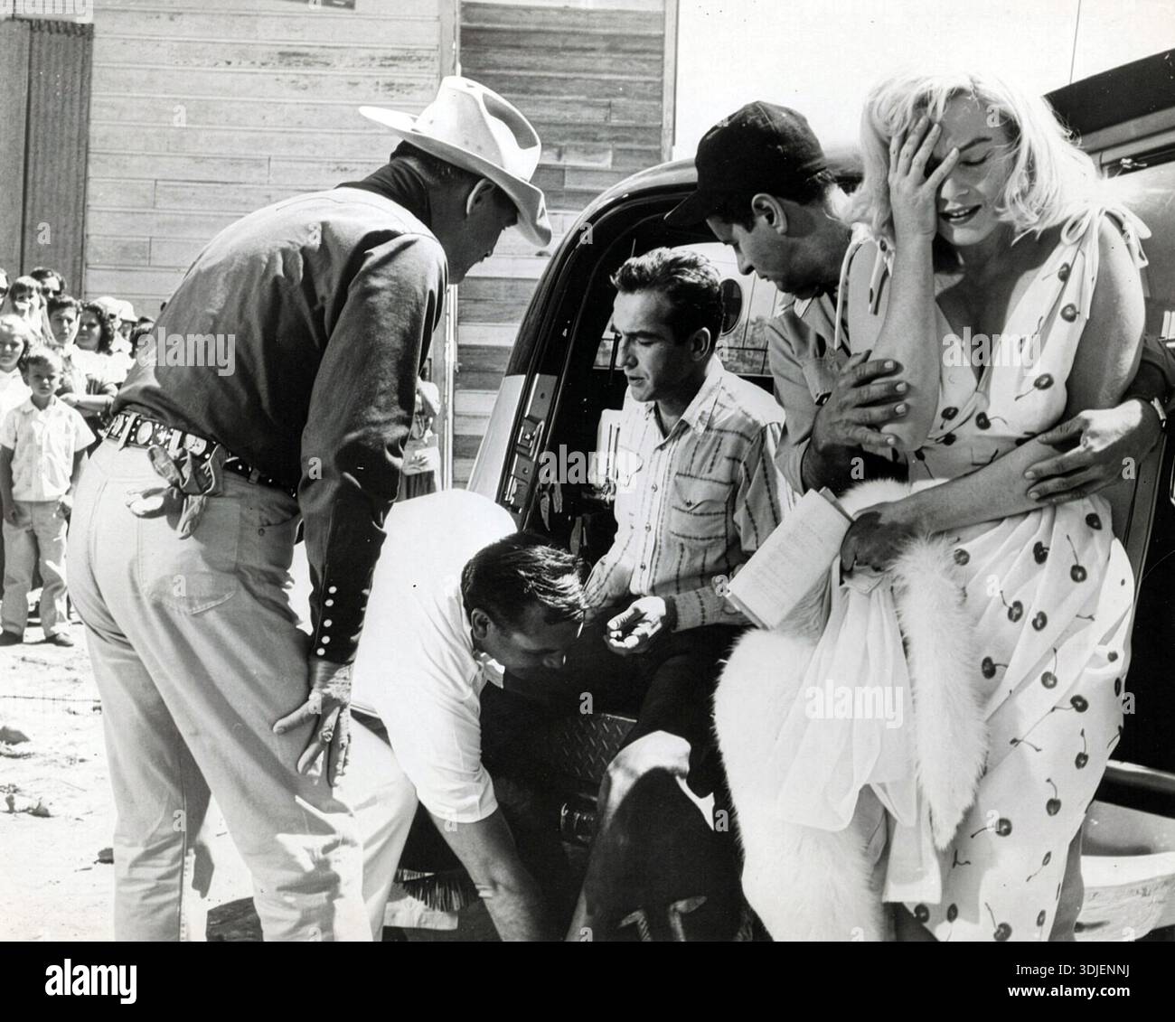 Cette photographie en noir et blanc de 1961 capture Marilyn Monroe sur le plateau de son dernier film, « les Misfits ». Elle semble affligée, tenant la tête, tout en étant réconfortée par un autre homme, alors que les membres de l'équipage et les curieux se rassemblent autour. Ce cliché franc révèle un moment de vulnérabilité lors de la production du film emblématique. Banque D'Images