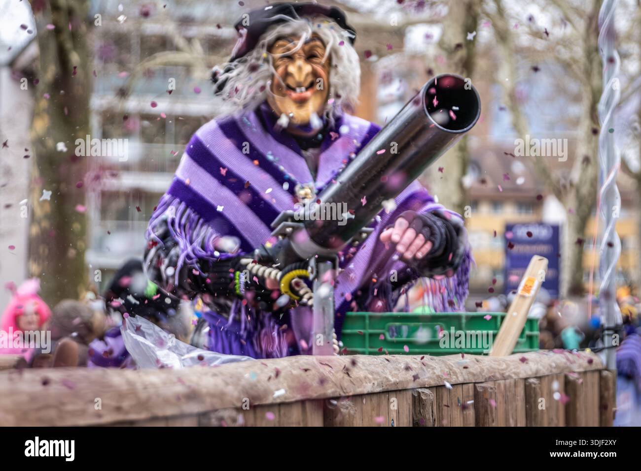 Zug, Suisse - 1er mars 2025 : interprète costumé en tenue de sorcière et masque Larve au défilé du carnaval d'hiver de Fasnacht avec un pistolet à confettis Banque D'Images