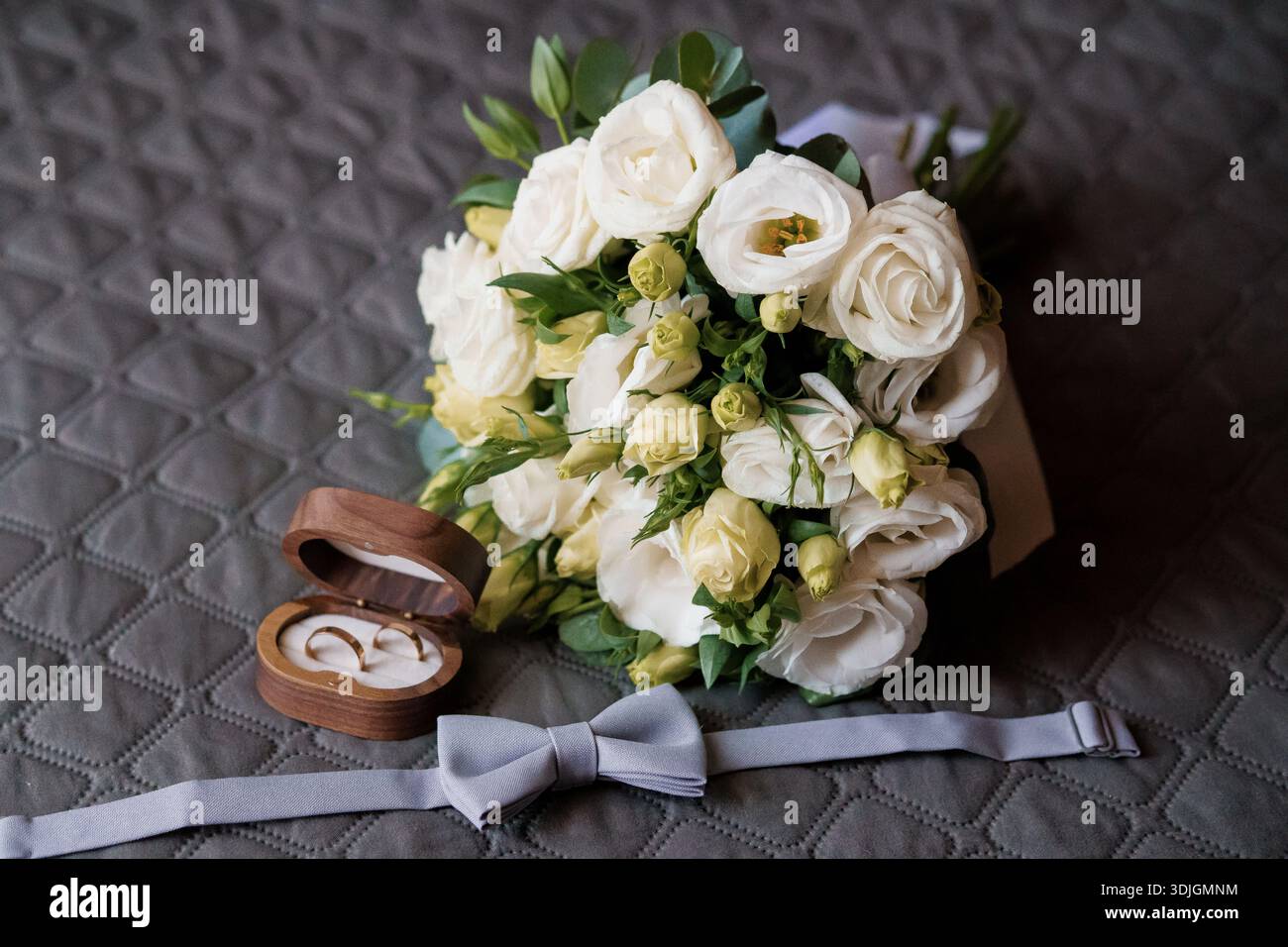 Un arrangement de mariage romantique avec un bouquet blanc luxuriant de roses et eustoma, une boîte à anneaux en bois avec des bandes de mariage en or, et un noeud papillon en argent sur Banque D'Images