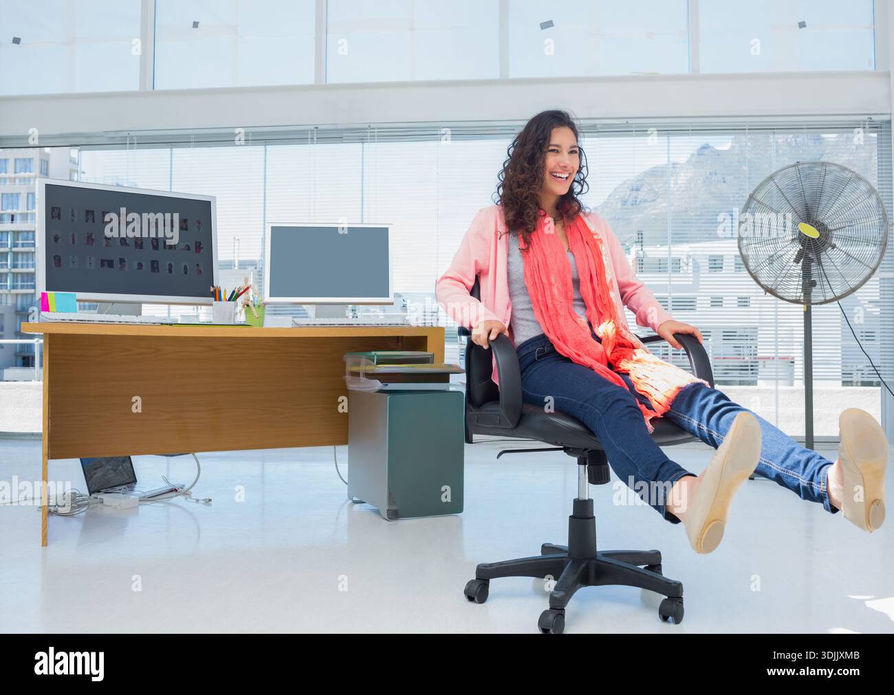 Chaise pivotante vide repose par un bureau en bois avec deux moniteurs, tasse à crayons, ventilateur dans le bureau. Paysage urbain, lumière du jour, moderne, espace de travail, urbain, minimaliste, Banque D'Images