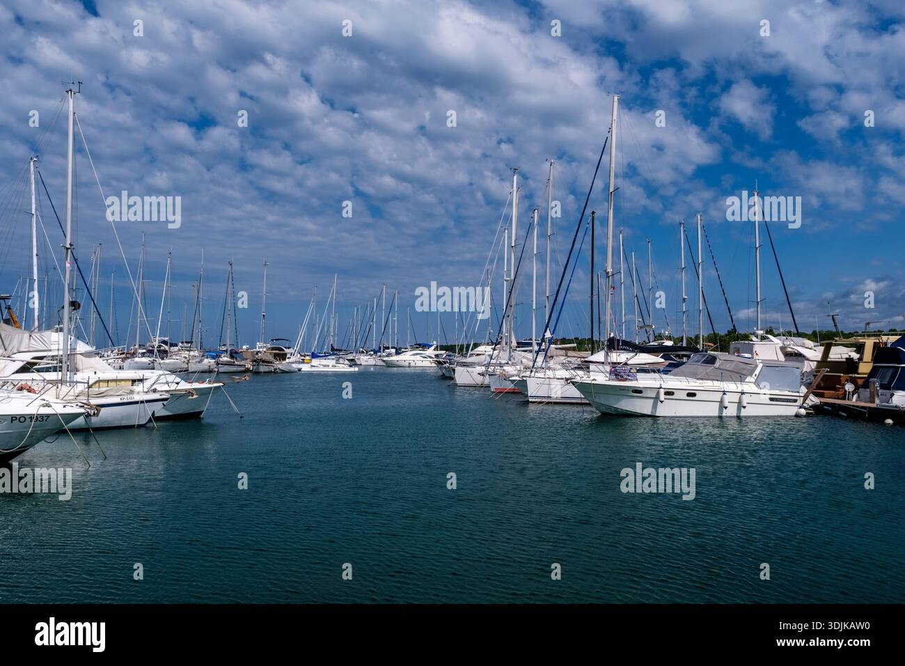 De nombreux voiliers et yachts blancs sont amarrés dans la marina de Cervar Porat sous un ciel bleu avec des nuages blancs éparpillés. Banque D'Images