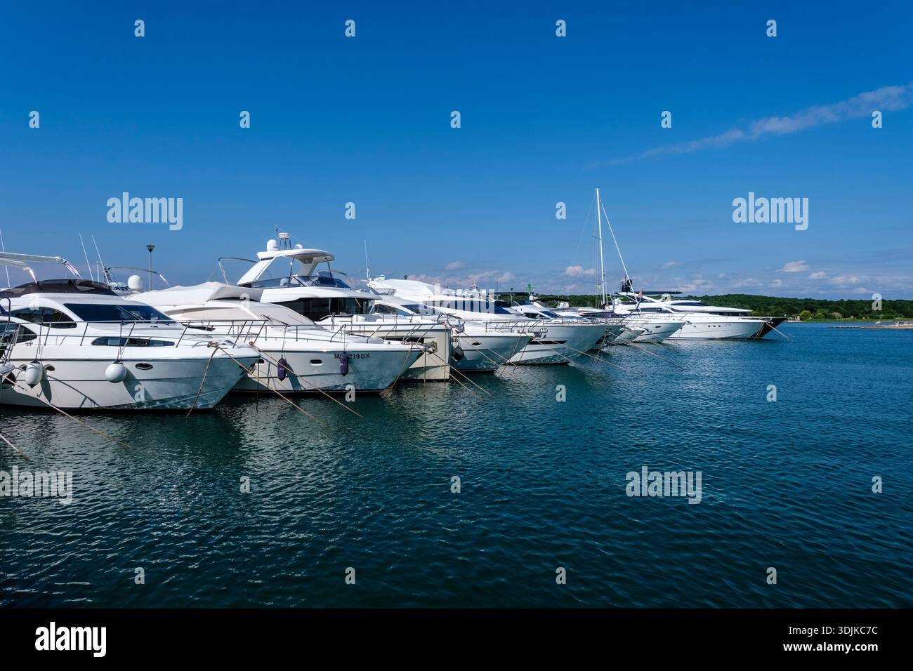 Des yachts blancs et des voiliers sont amarrés aux quais de Marina Funtana sous un ciel bleu clair. Banque D'Images