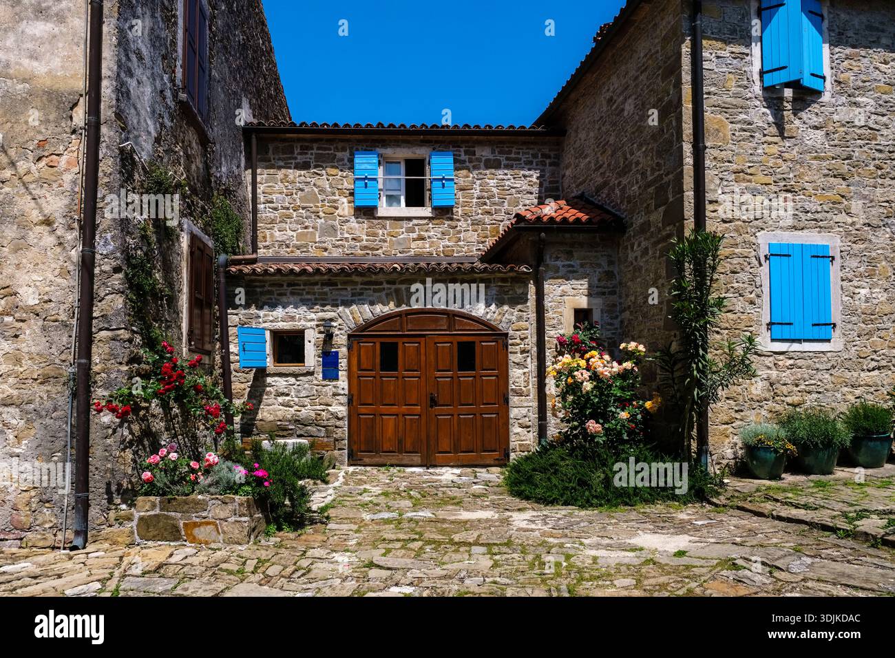 Maison traditionnelle en pierre avec volets bleus vifs et une grande porte en bois dans le centre historique de Grožnjan sous un ciel bleu clair. Banque D'Images