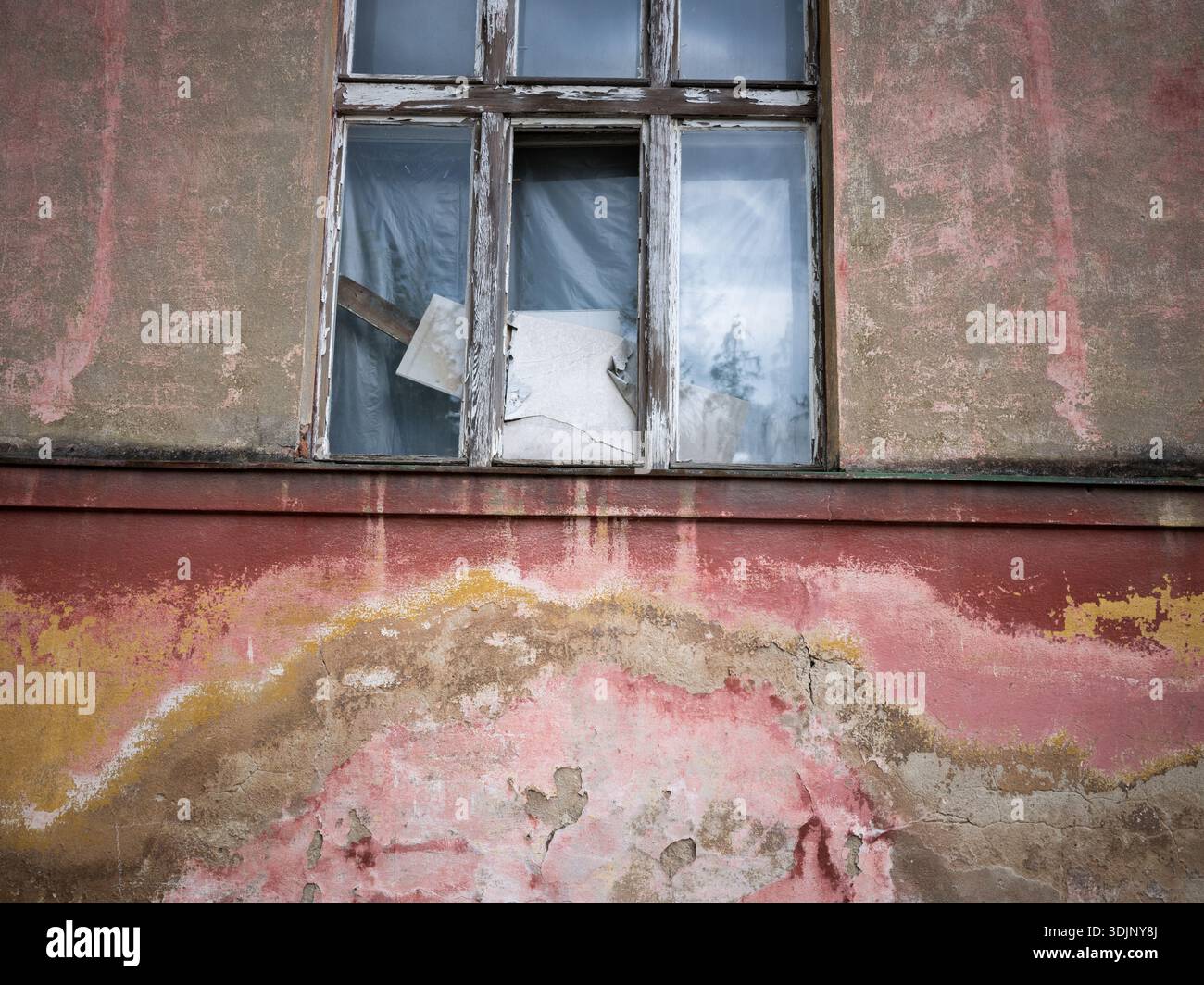 Vue détaillée d'une façade rouge et jaune altérée avec une grande fenêtre en bois sur un ancien bâtiment abandonné. Peinture écaillée et architecture en décomposition Banque D'Images