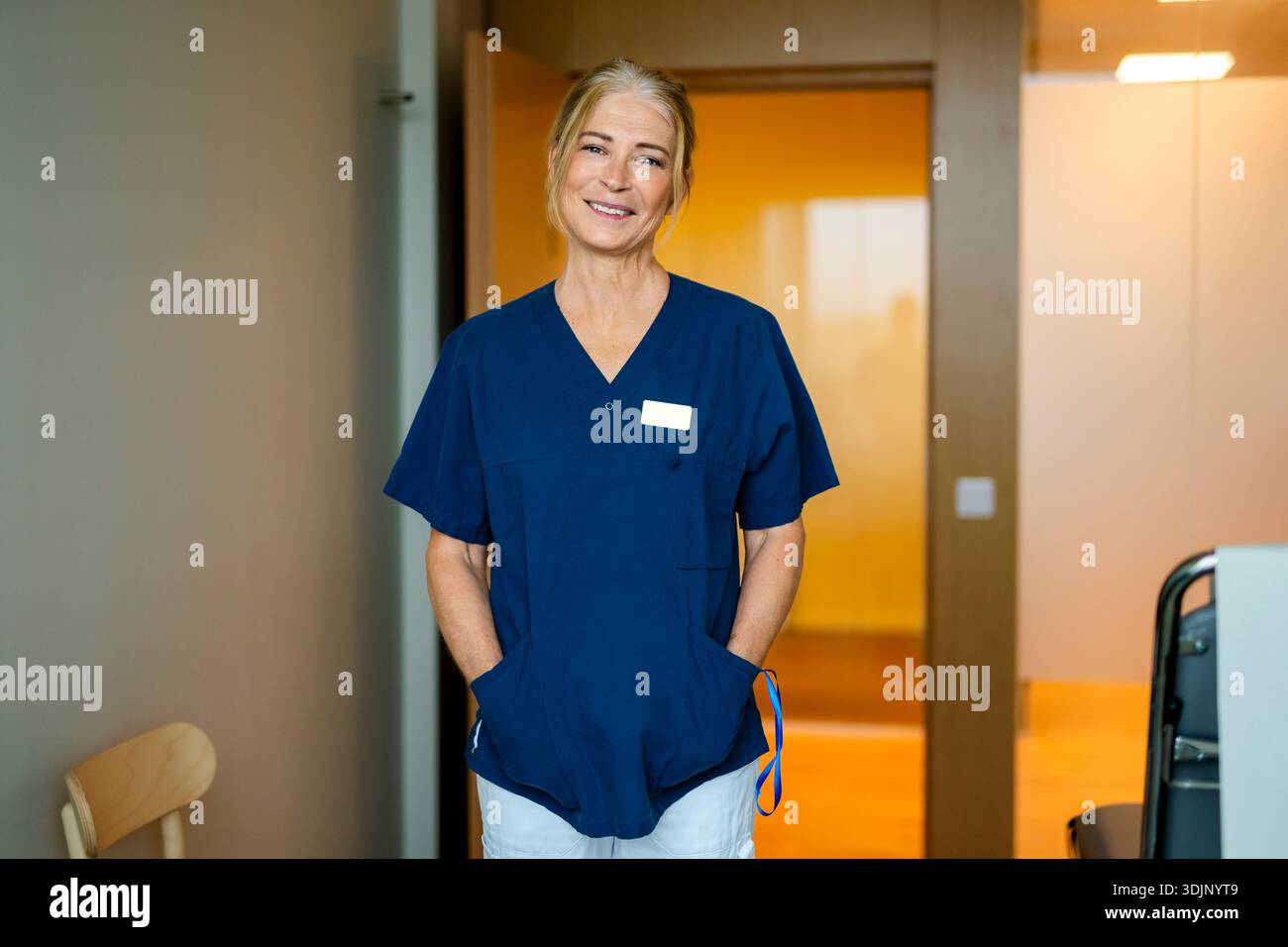 Portrait d'une professionnelle médicale senior souriante debout avec les mains dans les poches à la clinique Banque D'Images