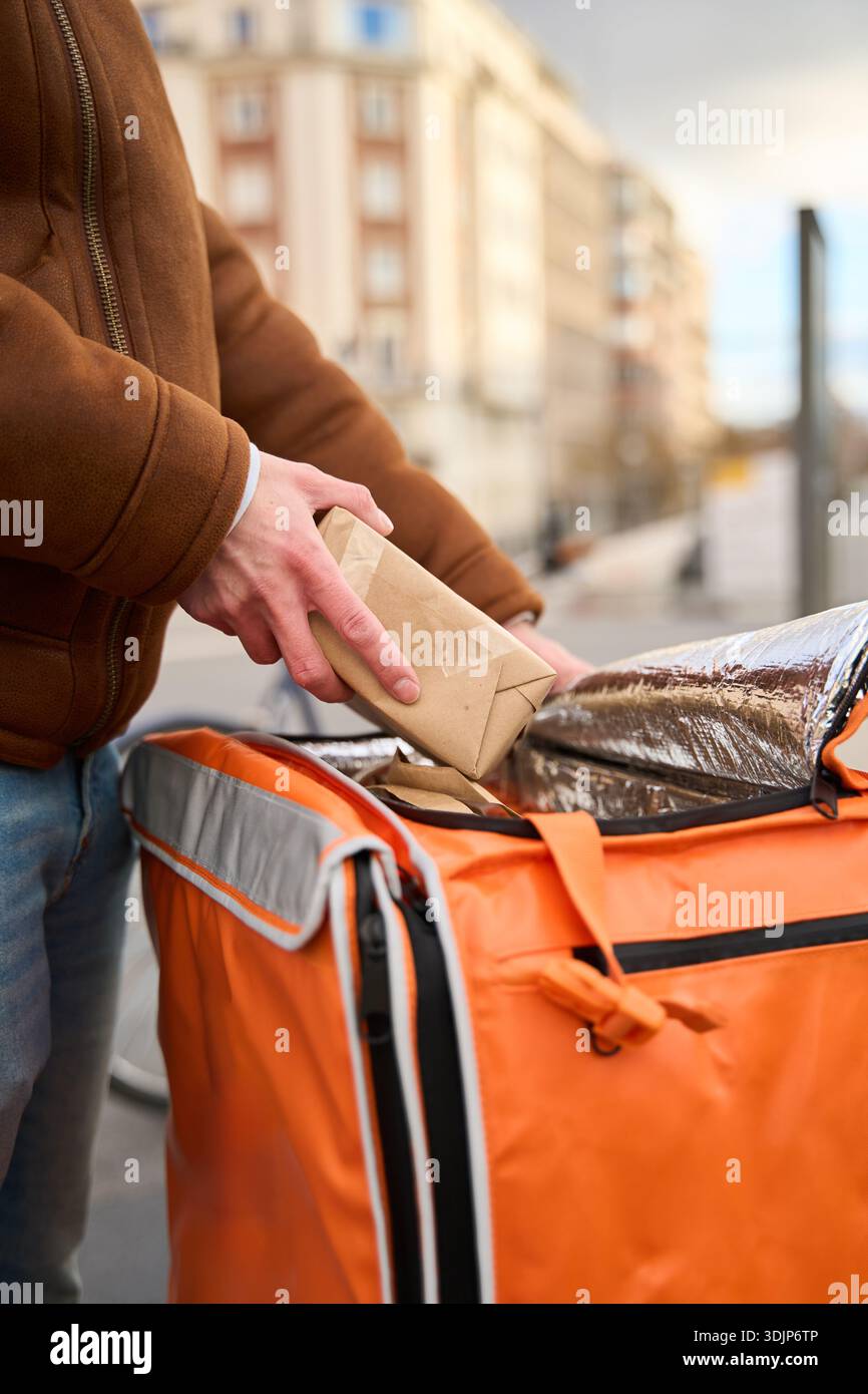 Personne plaçant un repas emballé dans un sac de livraison isotherme, prêt pour l'expédition urbaine. Concentrez-vous sur la logistique et le service modernes Banque D'Images