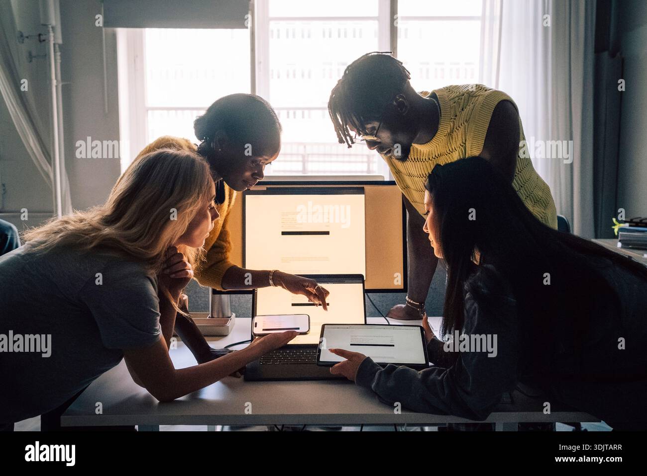 Professionnels créatifs féminins et masculins comparant des logiciels sur différents appareils tout en travaillant dans un bureau technique Banque D'Images