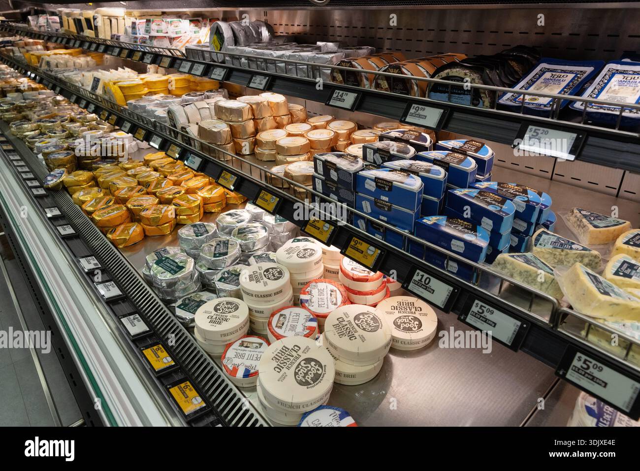 Assortiment de fromages présentés dans un comptoir frigorifique de supermarché, comprenant des fromages à pâte molle, à pâte dure et de spécialité emballés pour la vente au détail. Banque D'Images