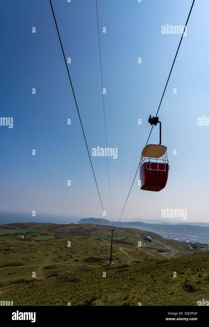 Cabine de téléphérique rouge suspendue à des câbles d'acier au-dessus des pentes herbeuses du promontoire de Great Orme Banque D'Images