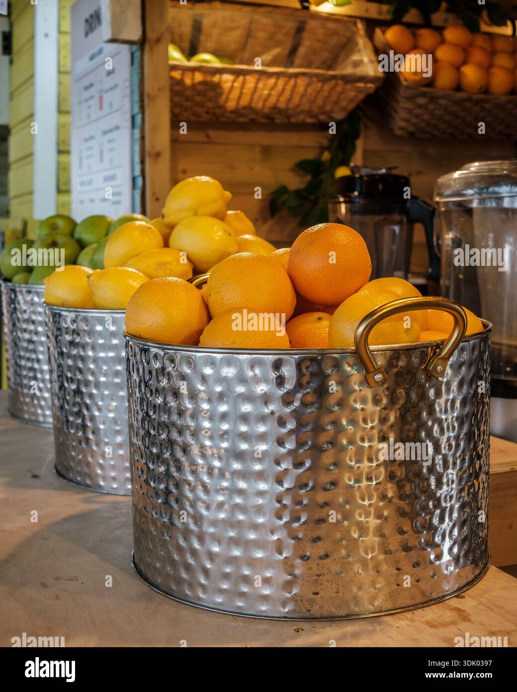 Oranges fraîches et pommes vertes exposées dans des seaux en métal dans un stand de jus de fruits de rue, prêt pour des boissons fraîchement pressées. Banque D'Images