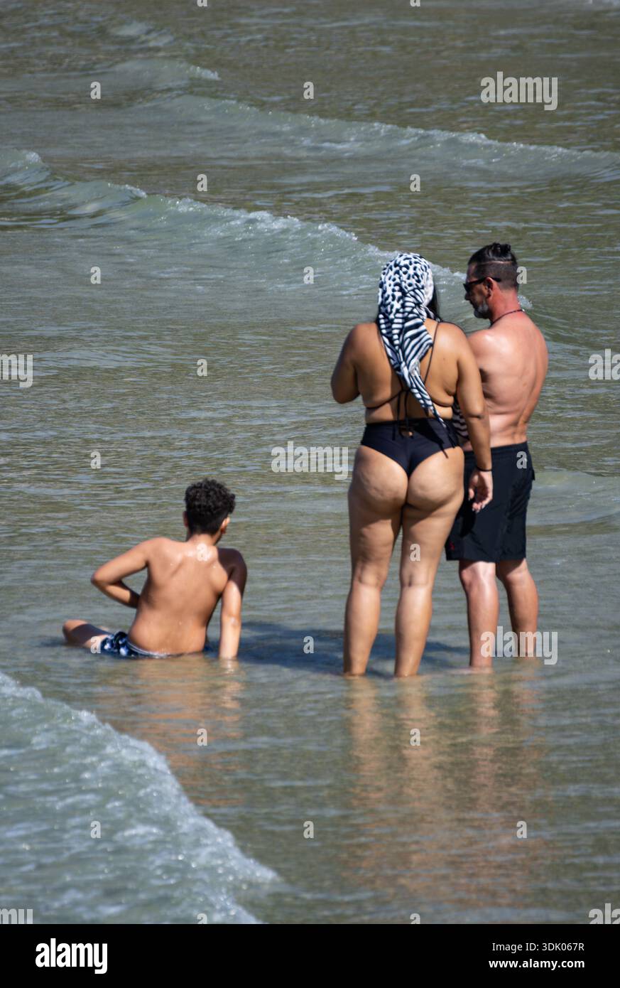 Couple d'âge moyen marche main dans la main à travers l'eau de mer calme profitant de la chaleur de la lumière du soleil et connexion romantique d'été. Banque D'Images
