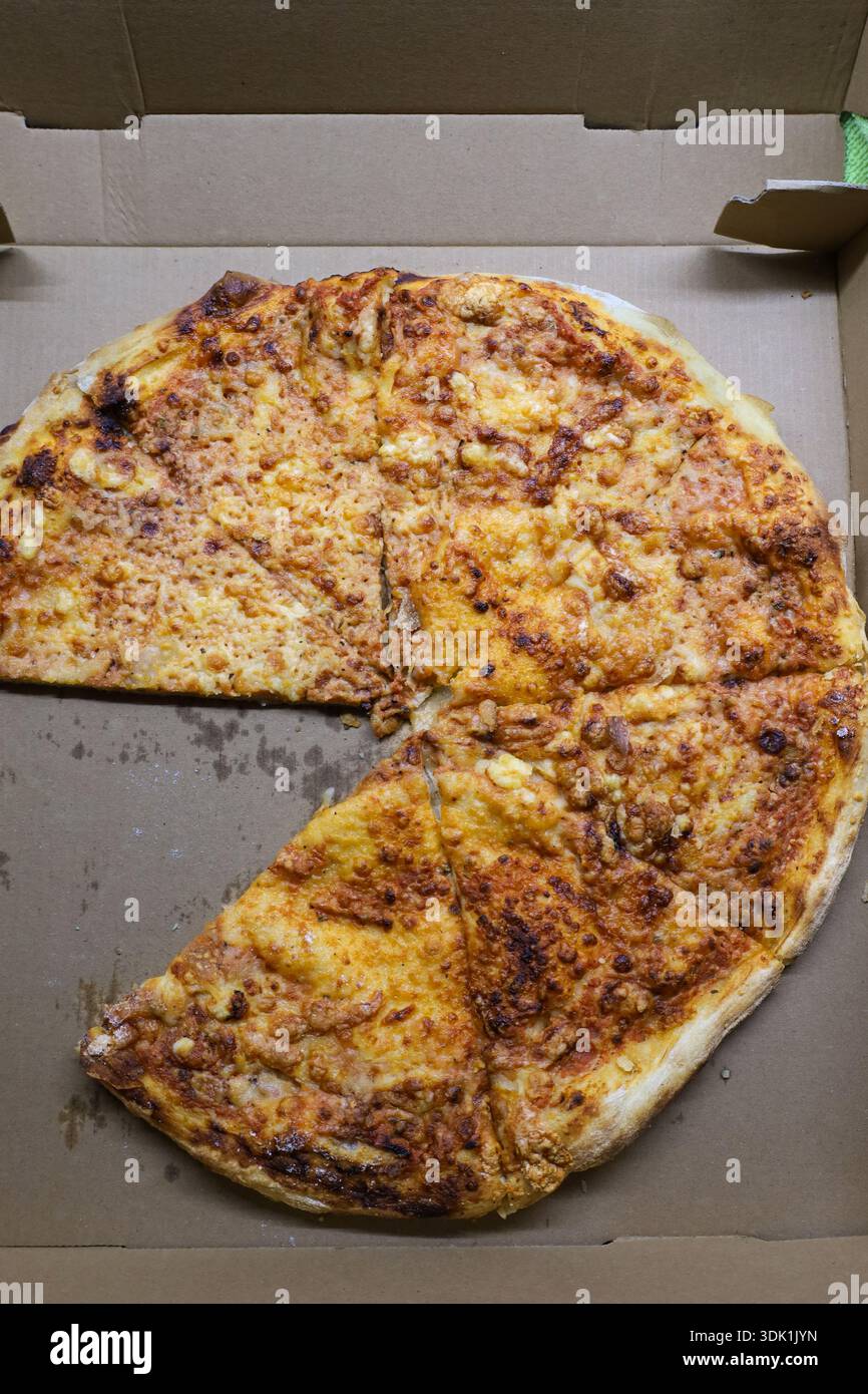 Vue aérienne d'une pizza au fromage dans une boîte de livraison en carton avec une tranche manquante, représentant un repas à emporter et décontracté. Banque D'Images