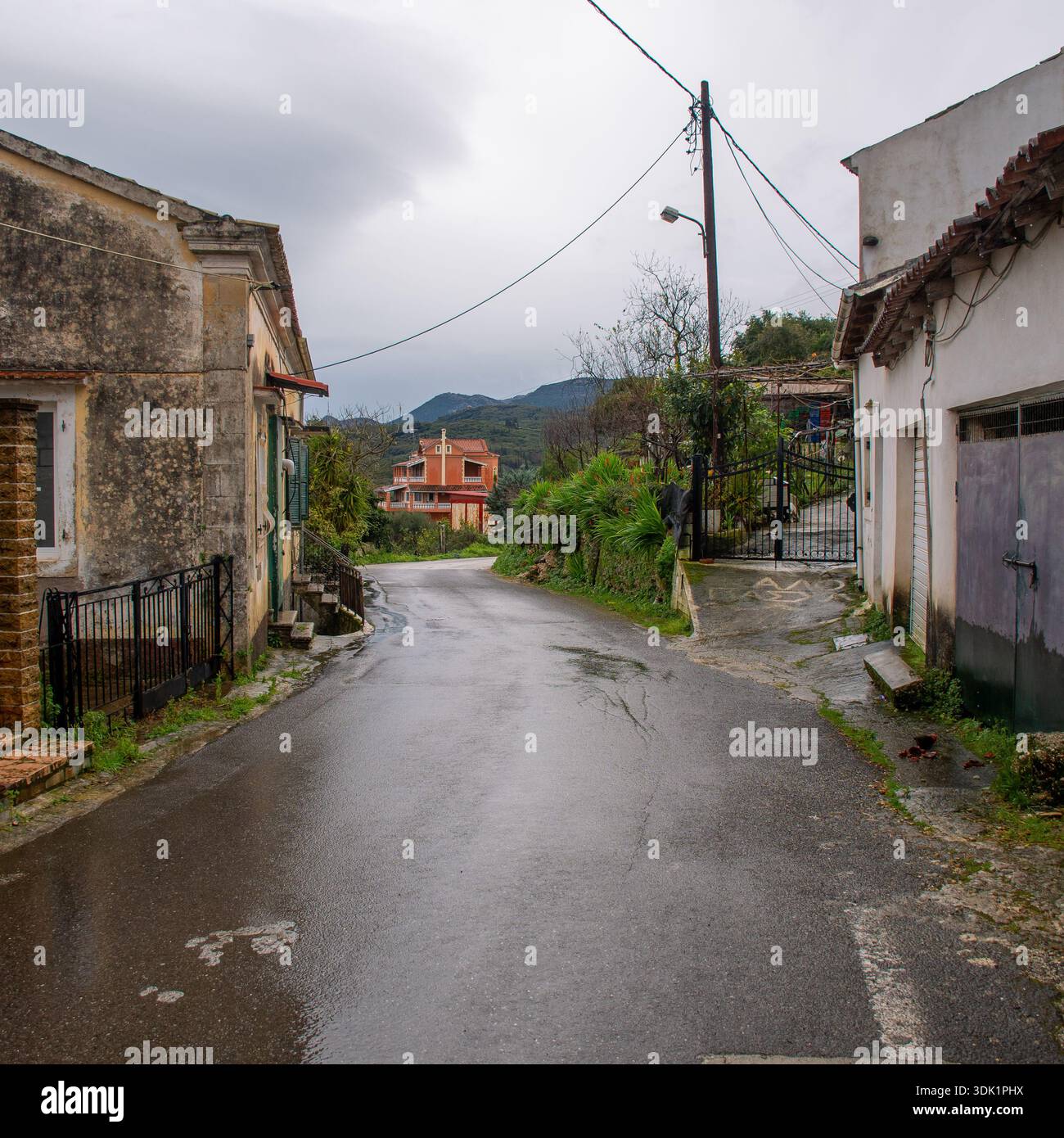 Récolte carrée d'une rue de village pluvieux traditionnelle à Agioi Douloi Corfou Grèce, montrant la route pavée humide, vieilles maisons en pierre, et l'architecture rurale sous-jacente Banque D'Images