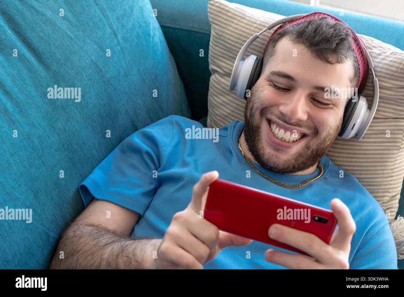 Un jeune homme latino sourit en regardant des séries télé sur son smartphone en mode paysage. Banque D'Images