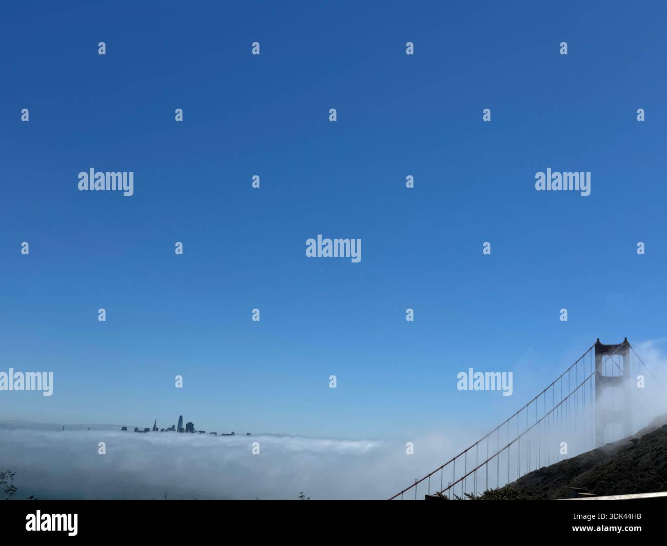 Tour du Golden Gate Bridge s'élevant au-dessus du brouillard côtier avec l'horizon de San Francisco faiblement visible au-delà de la couche marine. Banque D'Images