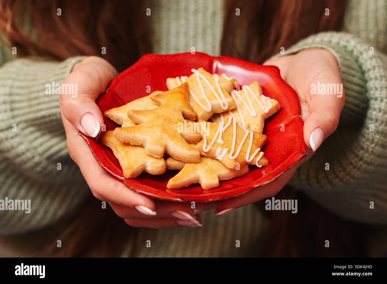 Biscuits de Noël sur plaque rouge tenus dans les mains gros plan. Bonbons faits maison. Dessert festif servant tradition. Nourriture de célébration hivernale. Banque D'Images