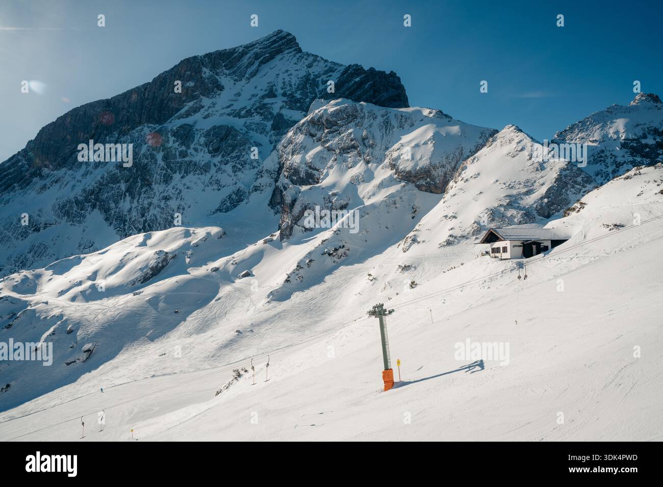 Un skieur descend une piste ensoleillée des Alpes bavaroises avec une cabane de montagne et des remontées mécaniques Banque D'Images