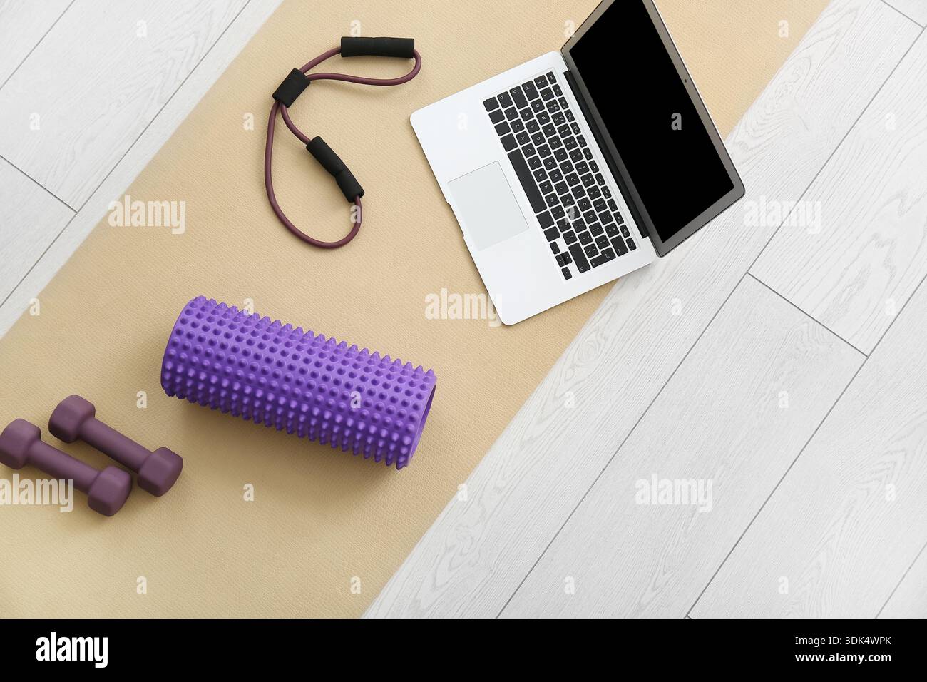 Rouleau en mousse avec ordinateur portable, haltères et extenseur de fitness sur tapis de yoga dans le salon, vue de dessus Banque D'Images