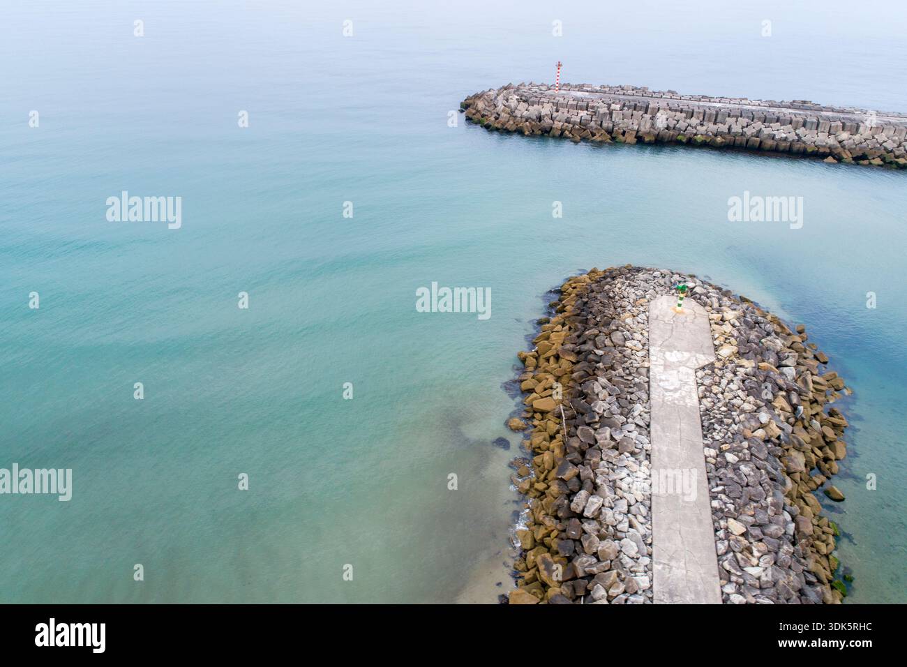 Vue aérienne d'une entrée du port avec deux brise-lames en pierre et un petit phare sur une mer calme Banque D'Images