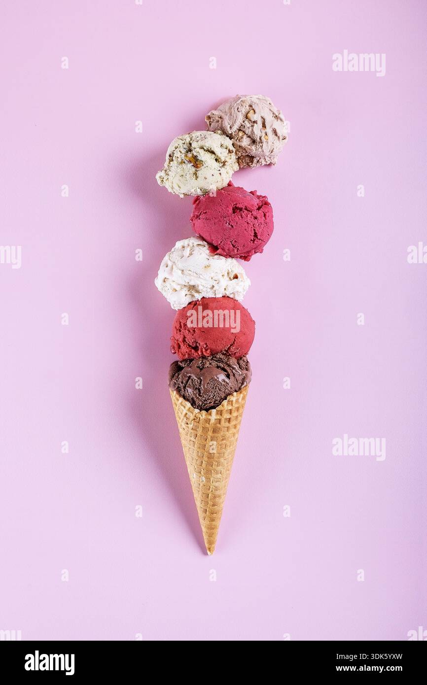 Cuillères à crème glacée assorties empilées sur un cône gaufré sur fond pastel Banque D'Images