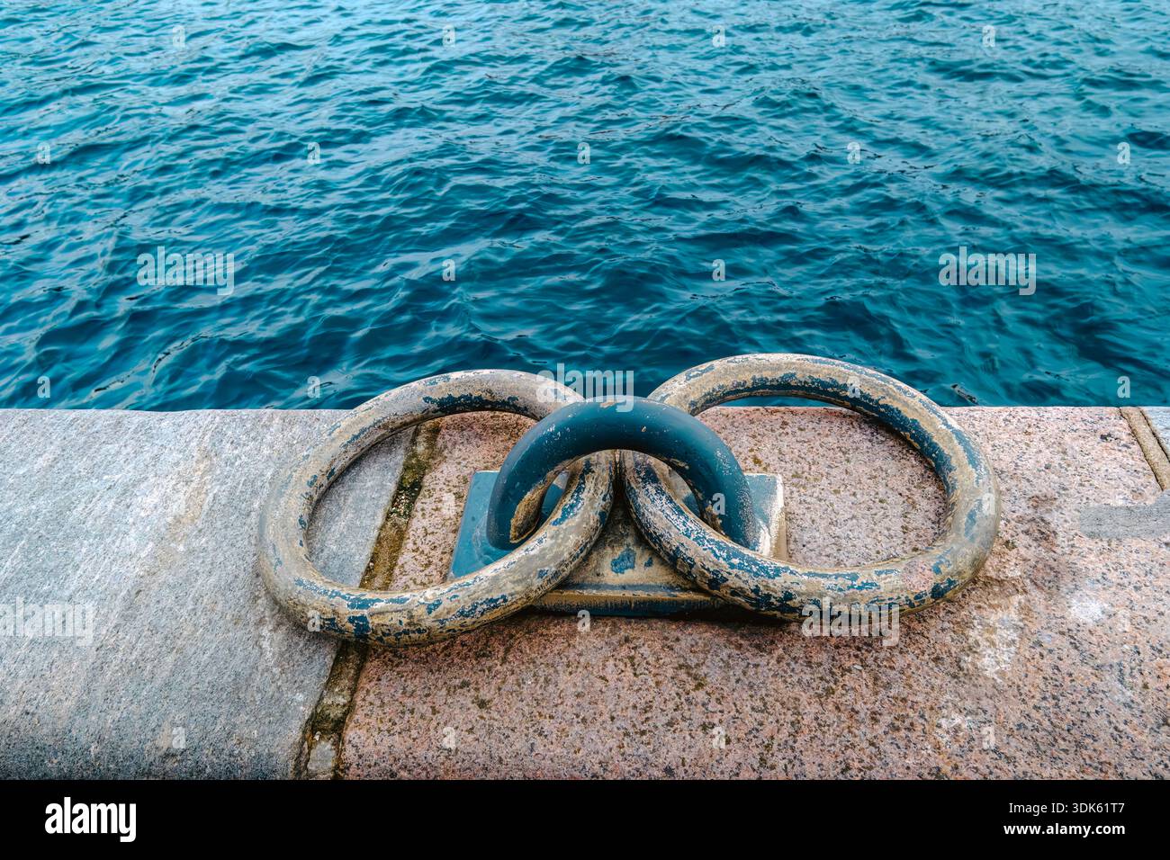 Vieux anneaux d'amarrage en métal sur Stone Pier, eau de mer sur fond, détail du port nautique Banque D'Images