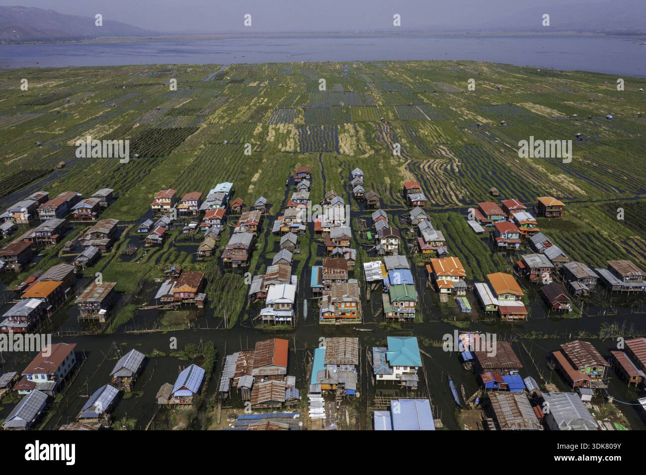 Vue aérienne de maisons sur pilotis avec des toits colorés s'élèvent de l'eau au milieu de jardins flottants sous un large ciel, Myayni Gone, Shan, Myanmar. Banque D'Images