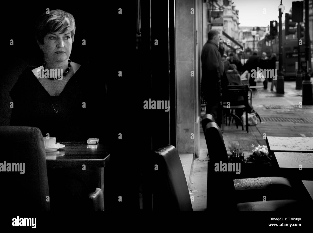 Femme dans un café regardant à travers la fenêtre, scène de rue, Londres, image N/B. Banque D'Images