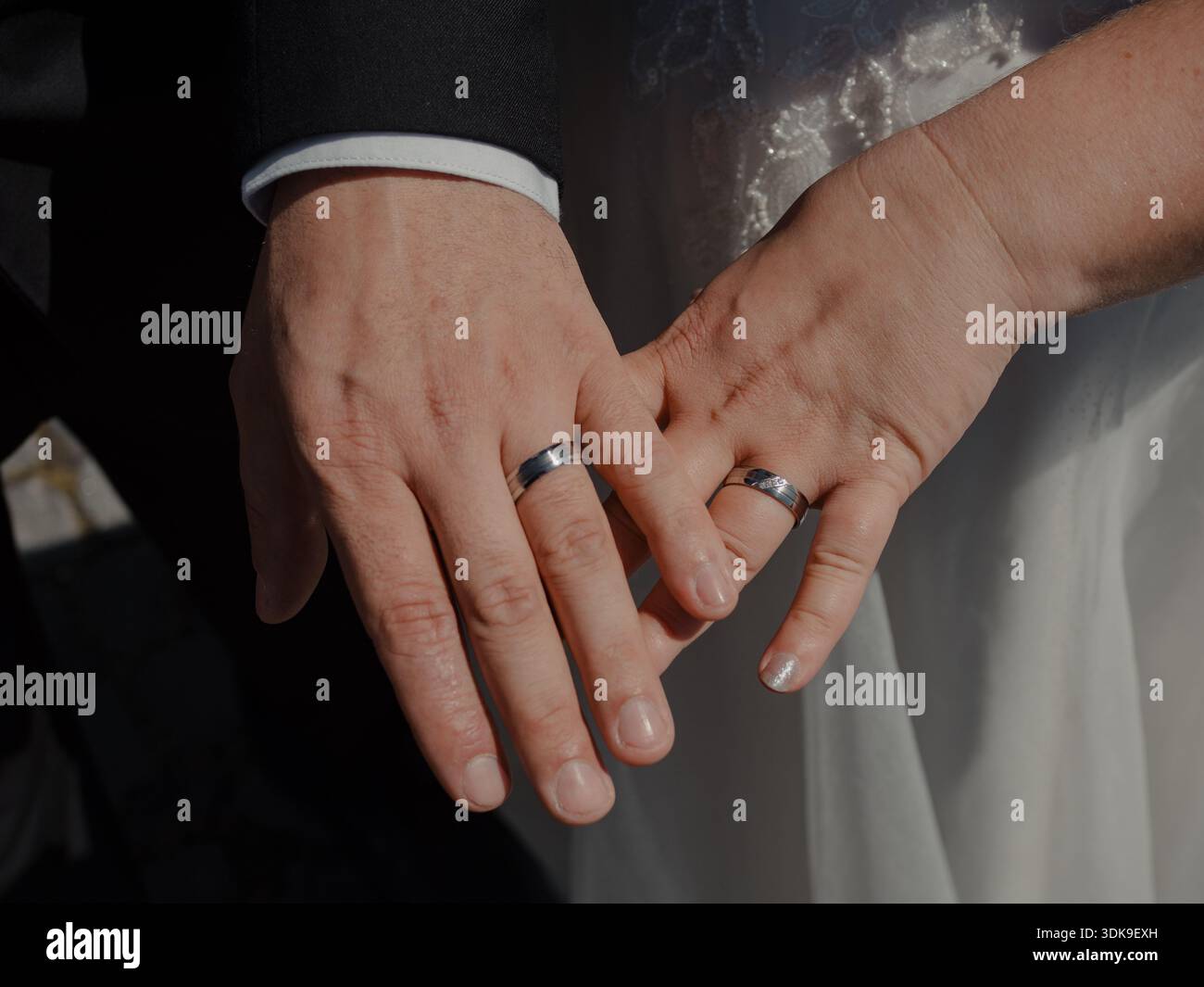 Gros plan de deux mains avec des anneaux de mariage reposant ensemble dans une lumière naturelle douce. Banque D'Images