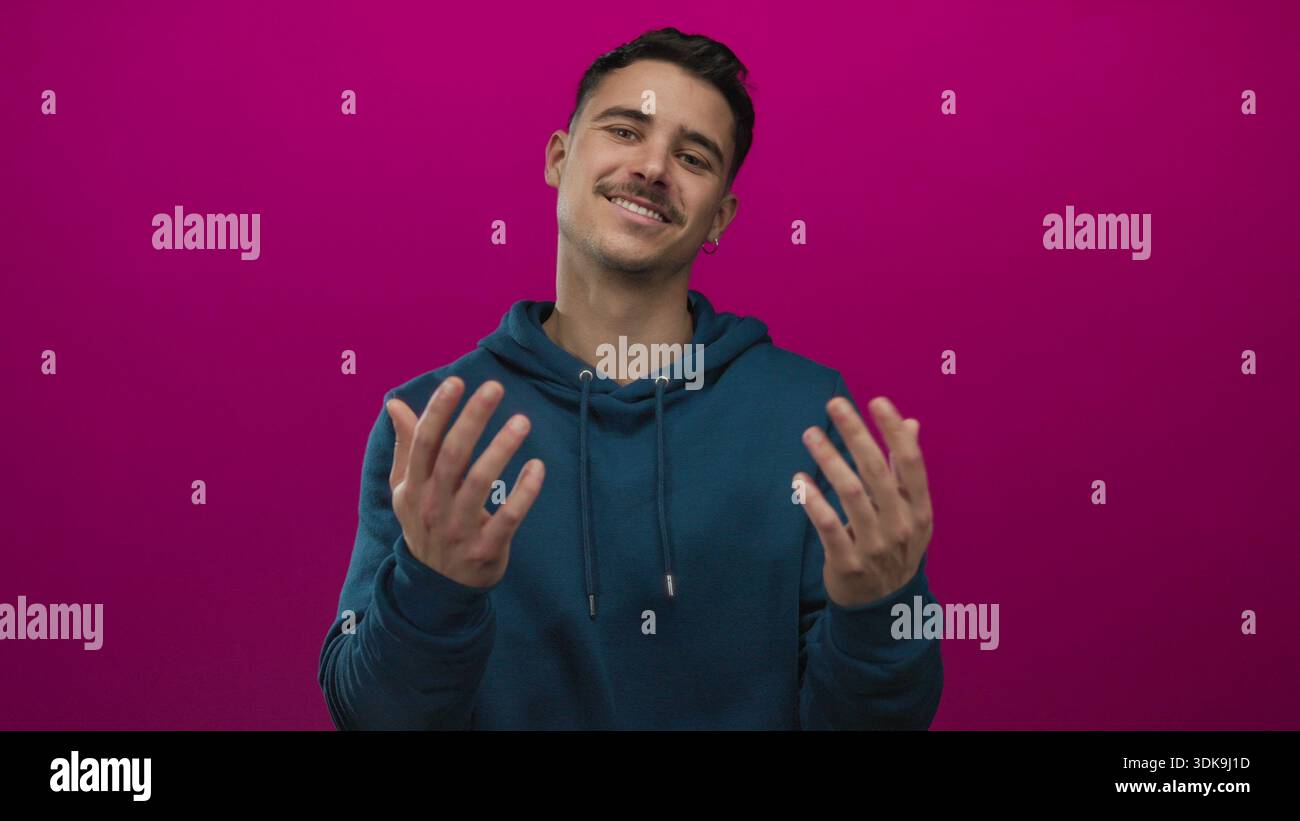 Les gestes d'un jeune homme hispanique viennent ici avec les mains sur un fond rose éclatant, apparaissant invitant et ludique dans un cliché de studio vif et isolé. Banque D'Images