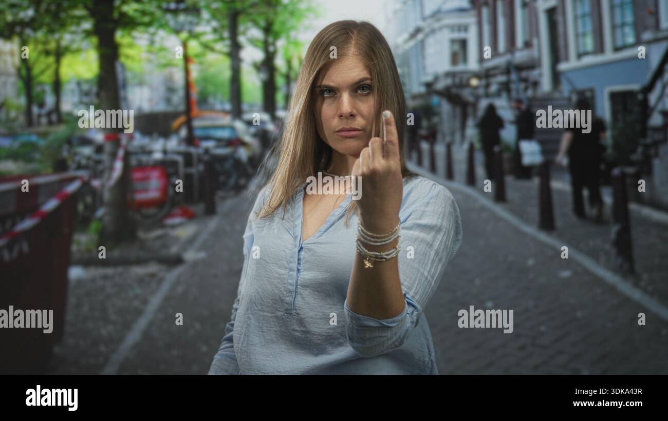 Jeune femme blonde se tient au milieu des vélos garés sur la rue pavée étroite retournant le majeur ; défi. Banque D'Images