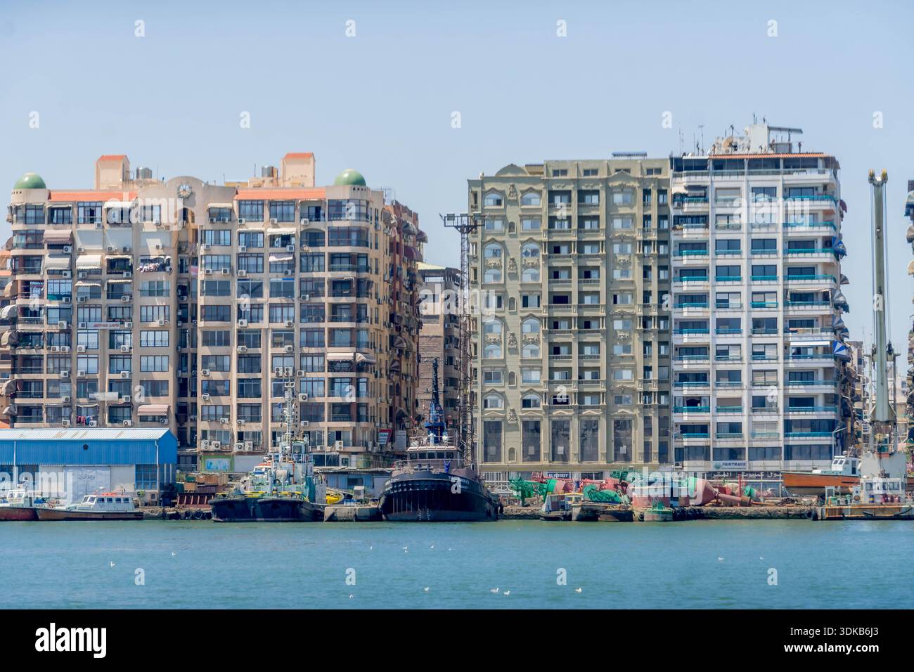Les appartements de grande hauteur bordent le front de mer de Port Saïd avec des bateaux de pêche amarrés, des hangars et des eaux portuaires calmes. Banque D'Images