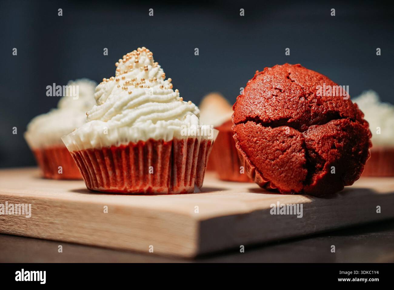 Gros plan de cupcakes en velours rouge sur une planche de bois, l'un recouvert de glaçage à la crème et de saupoudres. Banque D'Images
