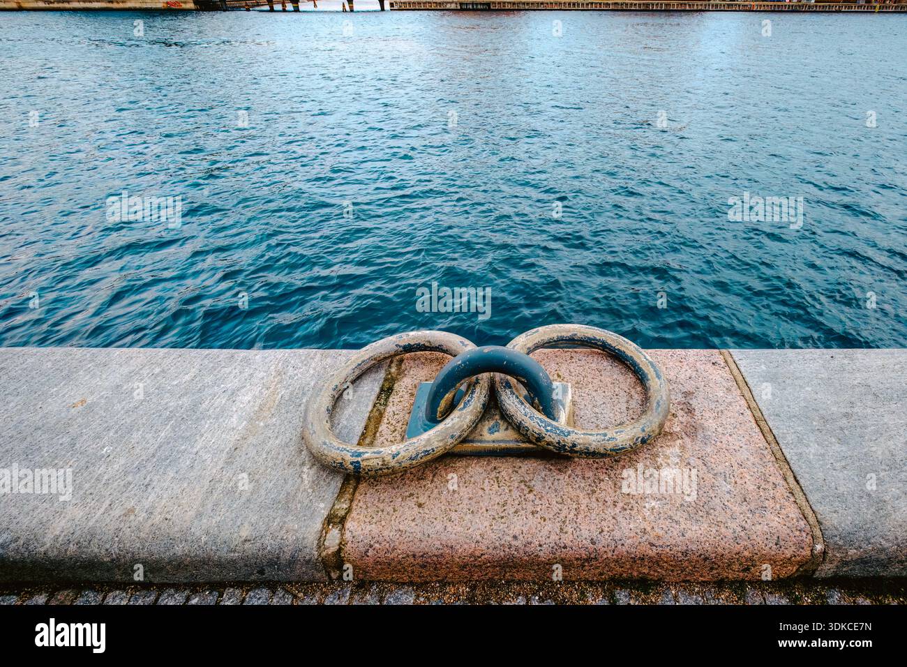 Anneaux d'amarrage en métal pour bateaux sur une jetée en pierre de granit, fond bleu d'eau, port Banque D'Images