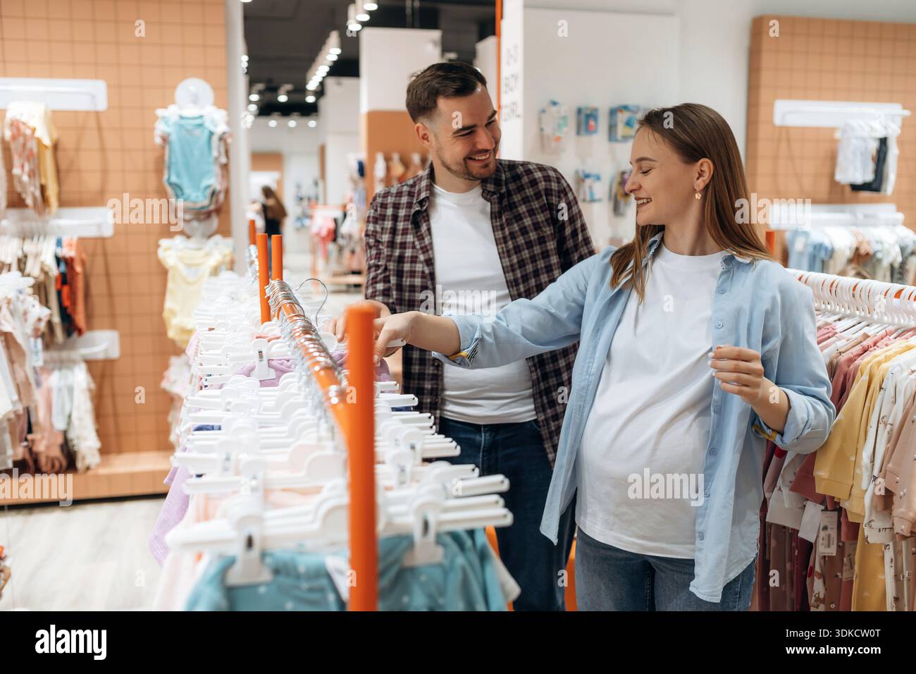 Expressions faciales positives. Femme enceinte avec homme sont dans le magasin de vêtements pour enfants. Banque D'Images