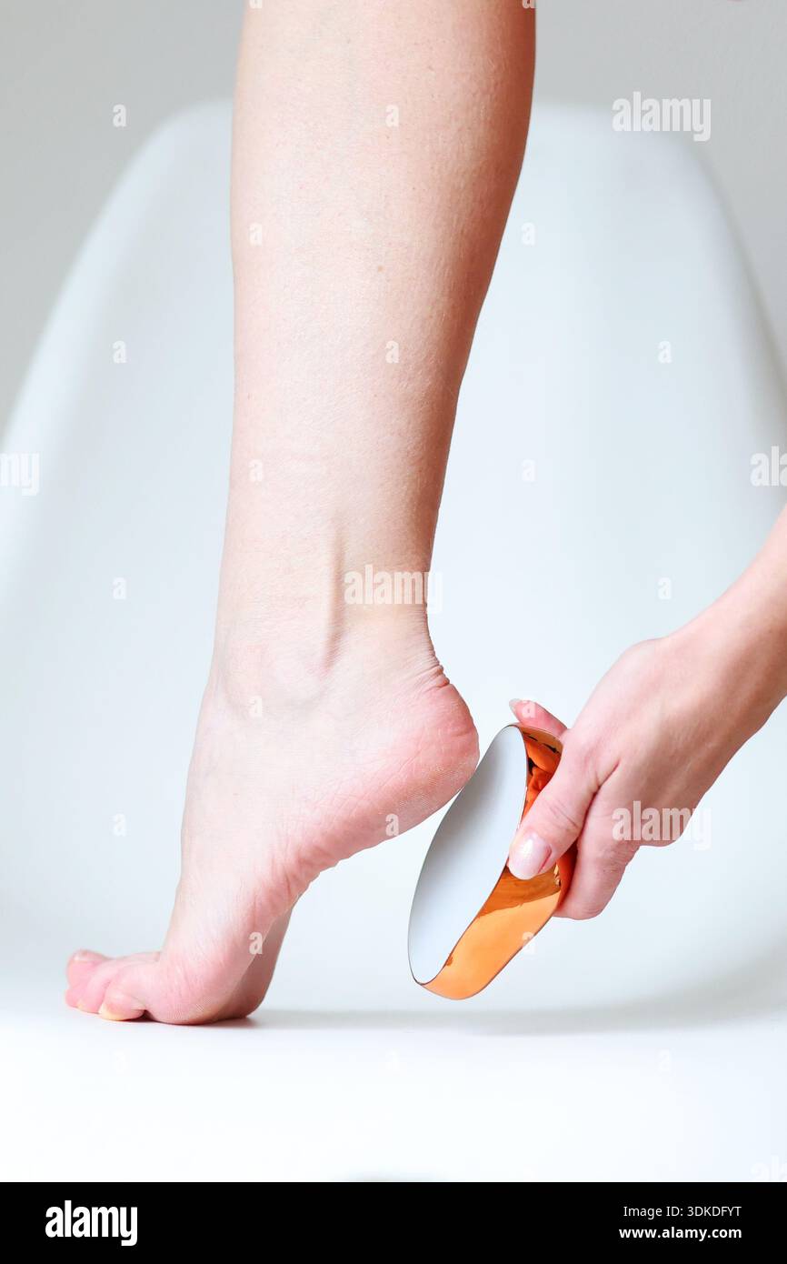 Concept de pédicure avec femme lissant les talons à l'aide de la lime de pied sur un fond minimal propre Banque D'Images