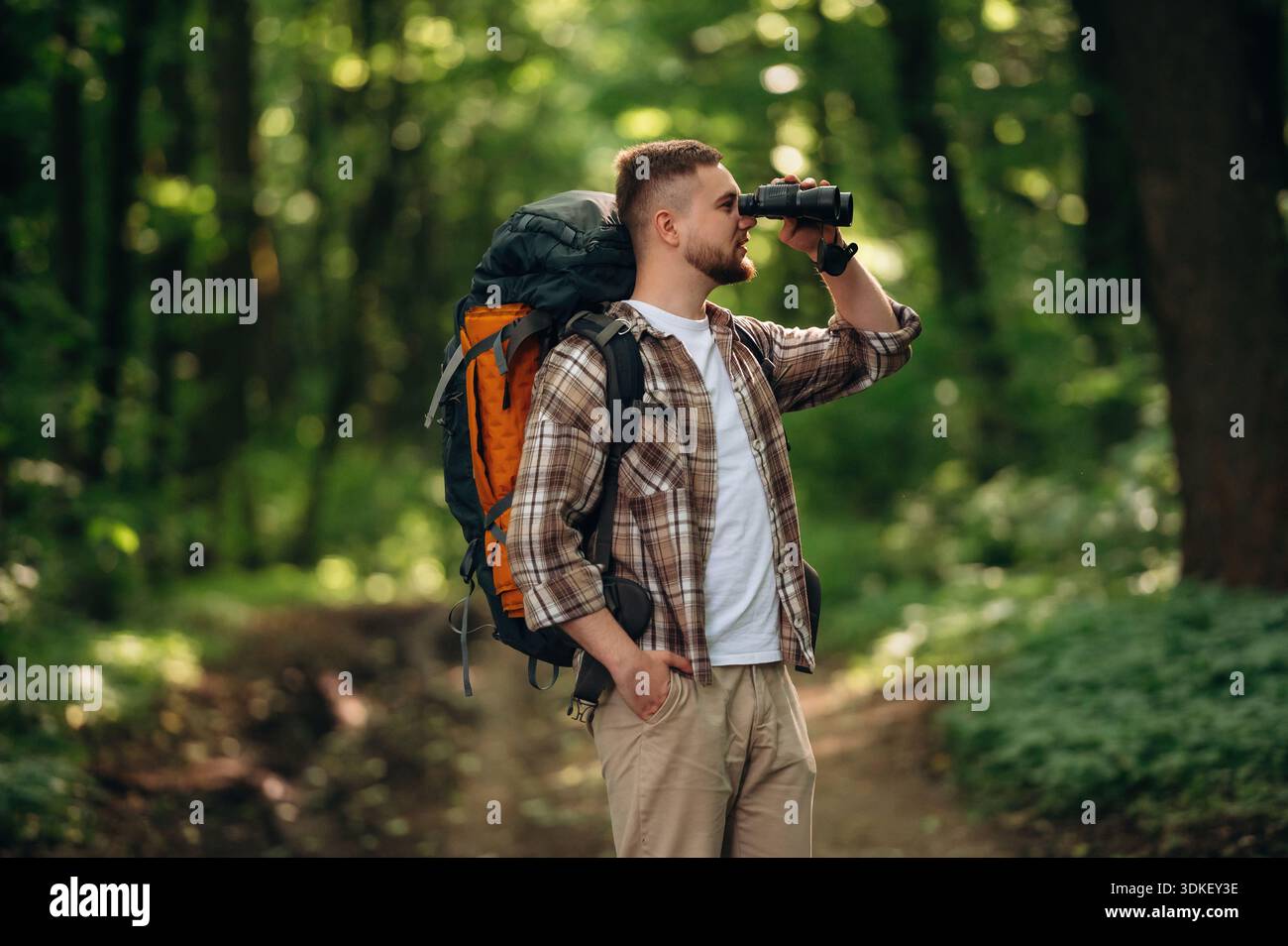 Vue latérale, debout, tenant des jumelles. Touriste masculin est avec sac à dos dans la forêt. Banque D'Images